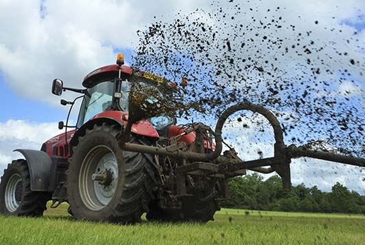 tractor spreads silage slurry on a farm field